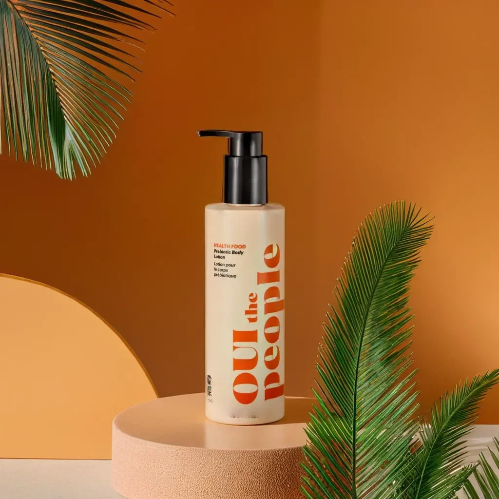 Bottle of 'Out the People' product on a round platform with palm leaves against an orange background