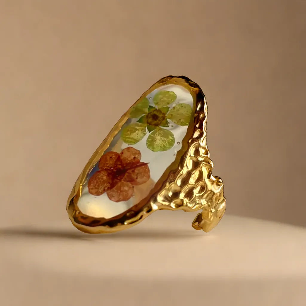 Woman Gold Ring with Pressed Flowers – Botanical Elegance
Close-up of gold ring with pink and green pressed flowers – woman gold ring
Side angle of floral gold plated ring – botanical jewelry for women
Adjustable gold ring with real flowers – gold plated ring romantic style
Ring styled on model hand – gold ring for woman with French elegance