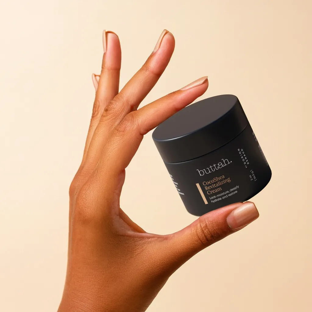 Jar of CocoShea Cream on a minimal shelf

Cream texture on fingertip, smooth and rich

Woman with melanin-rich skin applying cream to cheek

Close-up of hydrated, glowing skin after use